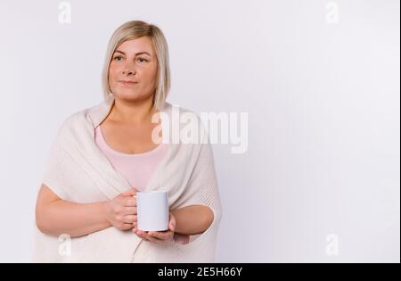 Ältere Frau schaut zur Seite und hält eine weiße Tasse Tee. Weißer Hintergrund und leerer Seitenraum. Stockfoto