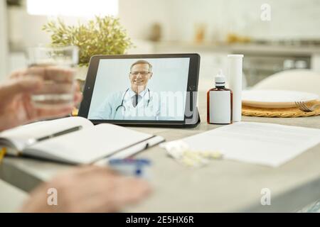 Schwarze Tablette mit dem Bild eines medizinischen Arbeiters lächelnd während Videoanruf an seinen eldelry Patienten Stockfoto