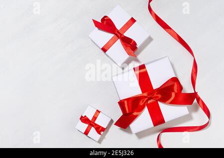 Weißes Geschenk in verschiedenen Größen Boxen mit roter Seidenschleife, Band auf weißem Holztisch, Draufsicht, Kopierraum, valentinstag Hintergrund. Stockfoto