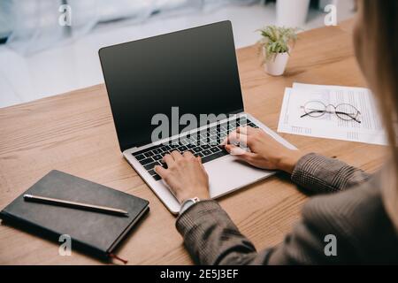 7/8-Ansicht von geschäftsfrau Tippen auf Laptop am Arbeitsplatz mit Dokumenten Stockfoto