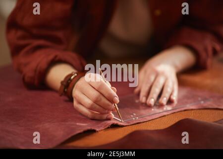Horizontaler Nahschuss aus schönen Händen von Handwerkerinnen, die Ledermaterial ausschneiden Stockfoto