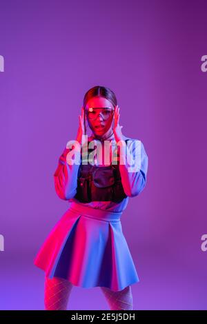 Junge Frau Anpassung Sonnenbrille und Blick auf Kamera auf lila Stockfoto