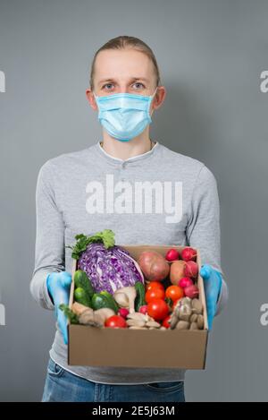 Mann Kurier liefert frisches Gemüse in einem Papierkarton in Sichere Maske und Handschuhe während Coronavirus Quarantäne Stockfoto