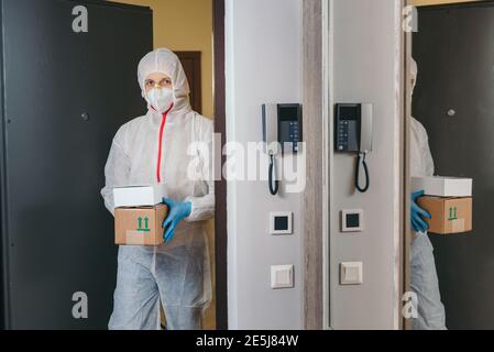 Mann hält Papierkiste mit Waren in medizinischen Handschuhen und Schutzmaske, kopieren Raum. Sichere Lieferung per Kurier während Coronavirus Quarantäne. Stockfoto