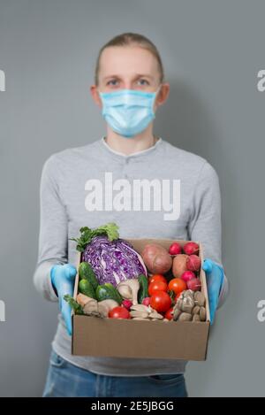 Mann Kurier liefert frisches Gemüse in einem Papierkarton in Sichere Maske und Handschuhe während Coronavirus Quarantäne Stockfoto