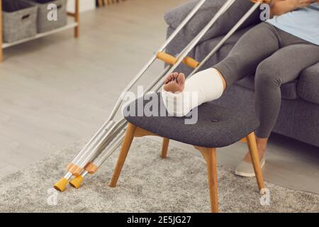 Nahaufnahme von Frauen gebrochenes Bein auf Stuhl in Besetzung und Metallkrücken Stockfoto