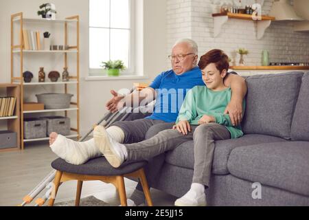 Älterer Mann mit einem gebrochenen Bein in einem Gipsabguss und erzählt Enkel die Geschichte, wie er Knöchel gebrochen. Stockfoto