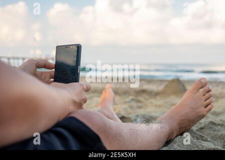 Die Beine des Mannes und er macht Fotos in der Nähe des Meeres Stockfoto