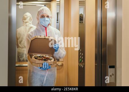 Mann Mitarbeiter in medizinischen Handschuhen und Schutzmaske liefern Pizza zu Hause während Virus Ausbruch. Speichern Sie Food-Service in Coronavirus Quarantäne Stockfoto