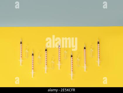 Spritzen und Ampullen mit transparenter Flüssigkeit auf trendigem gelben und grauen Hintergrund. Kosmetologie und Medizin Hintergrund. Coronavirus-Impfstoff-Konzept. Stockfoto