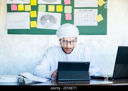 Der junge araber beschäftigt sich mit seiner Arbeit Zuhause mit hoher Konzentration mit seinem Laptop mit Stickbrett In seinem Büro Stockfoto