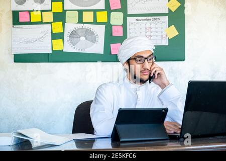 arabischer Mann, der sein Mobiltelefon benutzt, während er für die Kommunikation arbeitet Zwecke Stockfoto