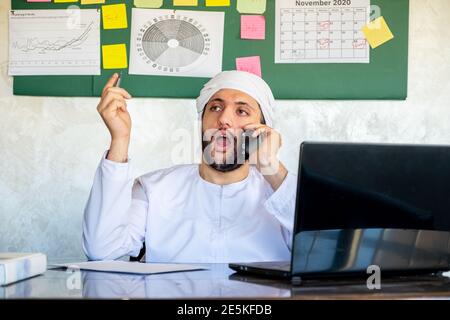 arabischer Mann, der sein Mobiltelefon benutzt, während er für die Kommunikation arbeitet Zwecke Stockfoto
