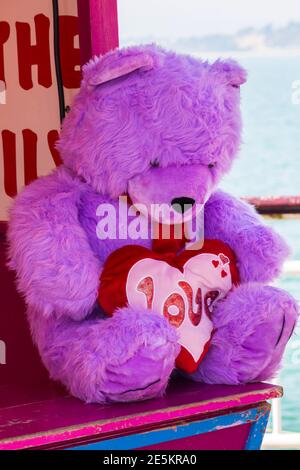 Purple Teddy Bear Holding Love Kissen traurig auf dem Messegelände Stand in Bournemouth, Dorset UK im April - allein zurückhaltend einsam forlorn Konzept Stockfoto