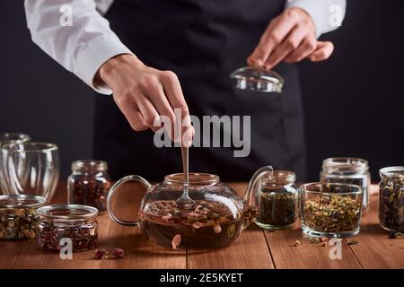 Der Barista rührt Rosenknospen mit einem Löffel in einer Teekanne Stockfoto