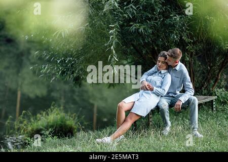 Junges Paar umarmt und sitzt am sonnigen Tag in der Nähe des Sees. Mann und Frau im Sommerurlaub. Konzept der schönen Familie. Selektiver Fokus. Stockfoto