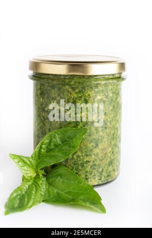 Pesto-Sauce in einem Glas isoliert mit frischen Basilikumblättern auf weißem Hintergrund. Traditionelle hausgemachte italienische Sauce Pesto und Basilikumblätter Stockfoto