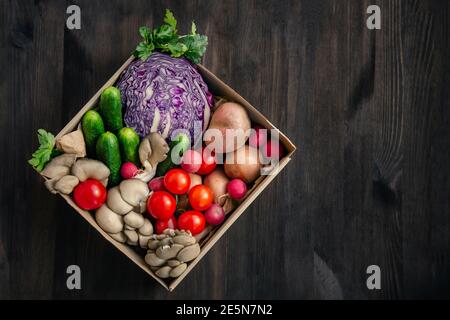 Frisches Gemüse in einer Pappschachtel liefern. Draufsicht auf gesundes vegetarisches Essen auf Holzhintergrund Stockfoto