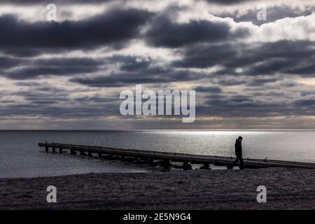 Insel Fehmarn, Deutschland. Januar 2021. Ein Mann geht unter dunklen Wolken am Südstrand. Kredit: Frank Molter/dpa/Alamy Live Nachrichten Stockfoto