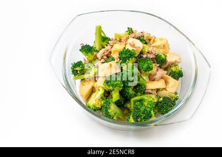 Thailändische hausgemachte Speisen, gebratener Brokkoli mit Tofu und gemahlenem Schweinefleisch, Speisen in einer durchsichtigen Glasschüssel auf weißem Hintergrund. Stockfoto