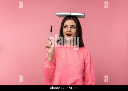 Foto von attraktiven Frau in Brille bedeckt ihren Kopf von Buch, schnell-witted Student arbeitet Studien online. Trägt lässige rosa T-Shirt weiße Hose Stockfoto