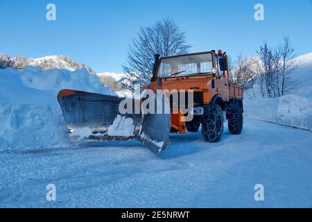 Orange Schneepflug LKW mit Schneeketten in einem gestoppt Ländliche verschneite Straße Stockfoto