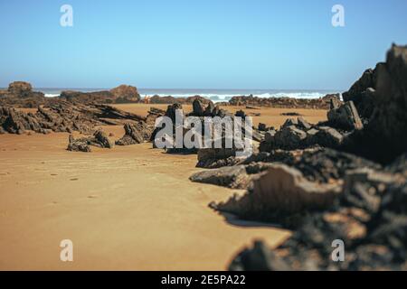 Vulkanische Felsformation am Sandstrand. Quadratische Steine an der Küste. Portugal, Küste der Algarve. Stockfoto