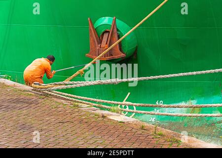 Männlicher Maler in orange insgesamt ist die Malerei der Anker Ein Schiff mit einer Farbrolle Stockfoto