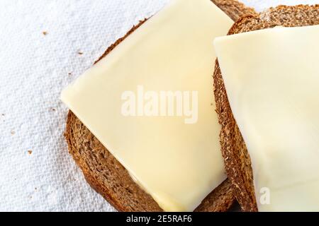 Draufsicht Nahansicht von zwei Scheiben leicht geröstetem Weizenbrot mit Margarine und Käse auf weißen Papiertüchern mit natürlichem Licht. Stockfoto