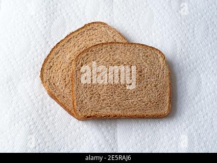 Blick von oben auf zwei Scheiben Weizenbrot auf weißen Papiertüchern mit Tageslicht. Stockfoto