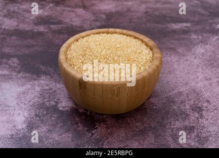 Holzschale gefüllt mit Rohzucker auf kastanienbraunem Hintergrund. Stockfoto