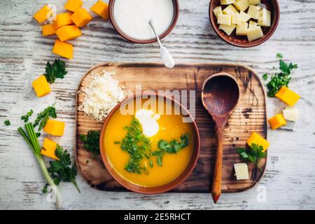 Schmackhaftes und gesundes vegetarisches Essen auf Holzhintergrund. Blick von oben auf die Kürbiscremesuppe, serviert mit Joghurt, Käse und Grün Stockfoto