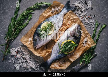 Roher dorado Fisch und Zutaten zum Kochen auf rustikalem Holzbrett und schwarzem Hintergrund, Draufsicht Stockfoto