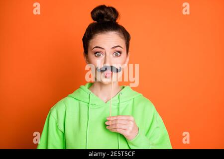 Foto von lustig überrascht junge Frau tragen grüne Kapuzenlippen Pouted halten Stick Schnurrbart isoliert lebendige orange Farbe Hintergrund Stockfoto