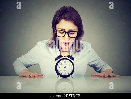 Ängstliche junge Frau, die am Tisch sitzt und den Wecker anschaut Stockfoto