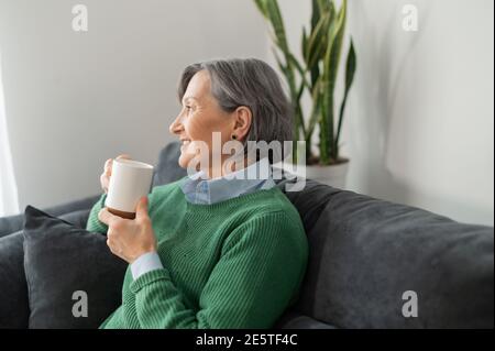 Ein Seitenansicht-Porträt einer älteren, grauhaarigen Dame, die in der Schlange wartet und ein kostenloses heißes Getränk genießt, sich ausruht und eine Kaffeepause hat Stockfoto