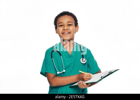 Afroamerikanischer Junge schreibt Gesundheitsbehandlung auf einem medizinischen Klemmbrett. Kind spielt Arzt, zukünftiger Beruf. Weißer Hintergrund Stockfoto