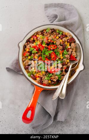 Traditionelle mexikanische Küche - Chili con Carne mit Hackfleisch Und Gemüse in Tomatensauce in Gusseisen einkochen Pfanne auf hellgrauem Schiefer oder Beton Bac Stockfoto