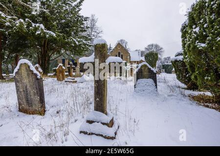 Friedhof, Kreuz und Grabsteine in St. John's Church in der Nähe von Woking, Diözese Guildford, Surrey, Südostengland nach einem starken Schneefall im Winter Stockfoto