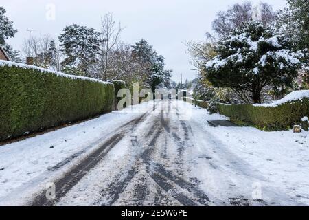 Auto- und Fahrzeugabreifenspuren im aufgewüllten Schnee, der in Hollybank Road, einer Vorstadtstraße in Hook Heath, nach einem Schneefall im Winter in Woking zum Slush wird Stockfoto