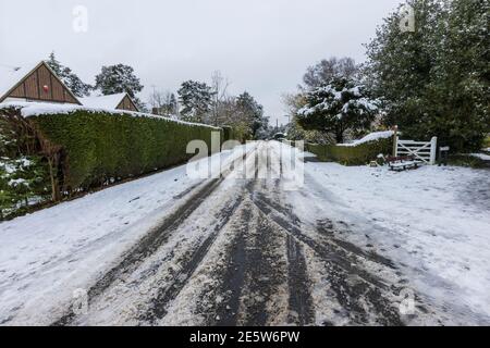 Auto- und Fahrzeugabreifenspuren im aufgewüllten Schnee, der in Hollybank Road, einer Vorstadtstraße in Hook Heath, nach einem Schneefall im Winter in Woking zum Slush wird Stockfoto