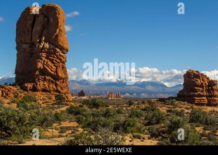 Seltsame hoch aufragende verwitterte Steinsäulen in der trockenen Landschaft des Archers National Park, Utah, mit den schneebedeckten Bergen im Hintergrund Stockfoto