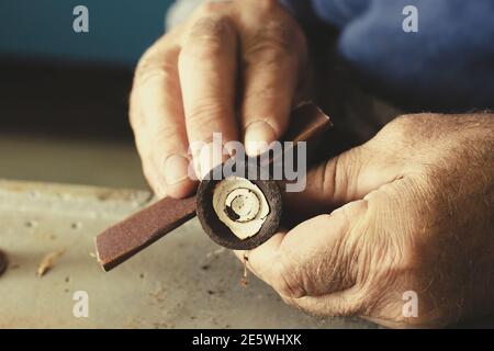 Die alten männlichen Hände des Meisters verarbeiten das Metallteil. Nahaufnahme der manuellen Arbeit. Stockfoto