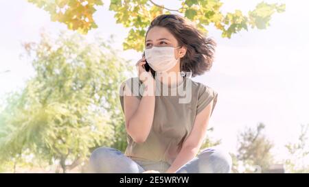 Junge glückliche Frau mit Gesichtsmaske reden am Telefon draußen. Neue Normalität nach Ausbruch des Coronavirus. Gesunde Lebensstile und Technologiekonzepte. Stockfoto