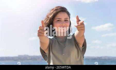 Junge schöne Frau tut DoppelDaumen nach oben am Meer. Das alles zu gestikulieren ist großartig. Außenaufnahmen. Stockfoto