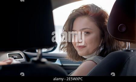 Junge schöne Frau in Maske sitzt auf dem Beifahrersitz im Inneren eines Autos lächelt Blick über Schulter auf die Kamera. Stockfoto