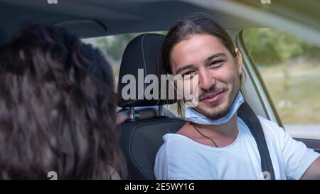 Glückliches junges Paar, Freunde mit Gesichtsmasken sitzen im Auto und reden sich gegenseitig. Roadtrip in neuer Normalität. Corona-Virus-Pandemiekonzept. Stockfoto