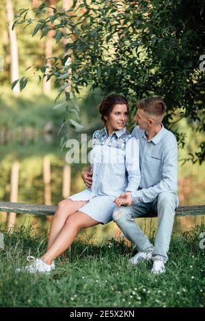 Junges Paar umarmt und sitzt am sonnigen Tag in der Nähe des Sees. Mann und Frau im Sommerurlaub. Konzept der schönen Familie. Selektiver Fokus. Stockfoto