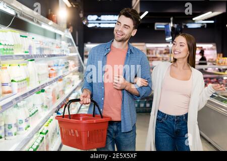 Lächelndes Paar mit Einkaufskorb Blick auf Lebensmittel auf verschwommen Vordergrund im Supermarkt Stockfoto