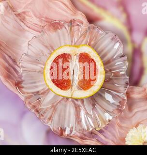 Die Hälfte einer geschnittenen reifen saftigen Grapefruit auf einer transparenten Platte auf einem strukturierten, malerischen rosa Hintergrund. Gesunde Bio-Früchte Stockfoto